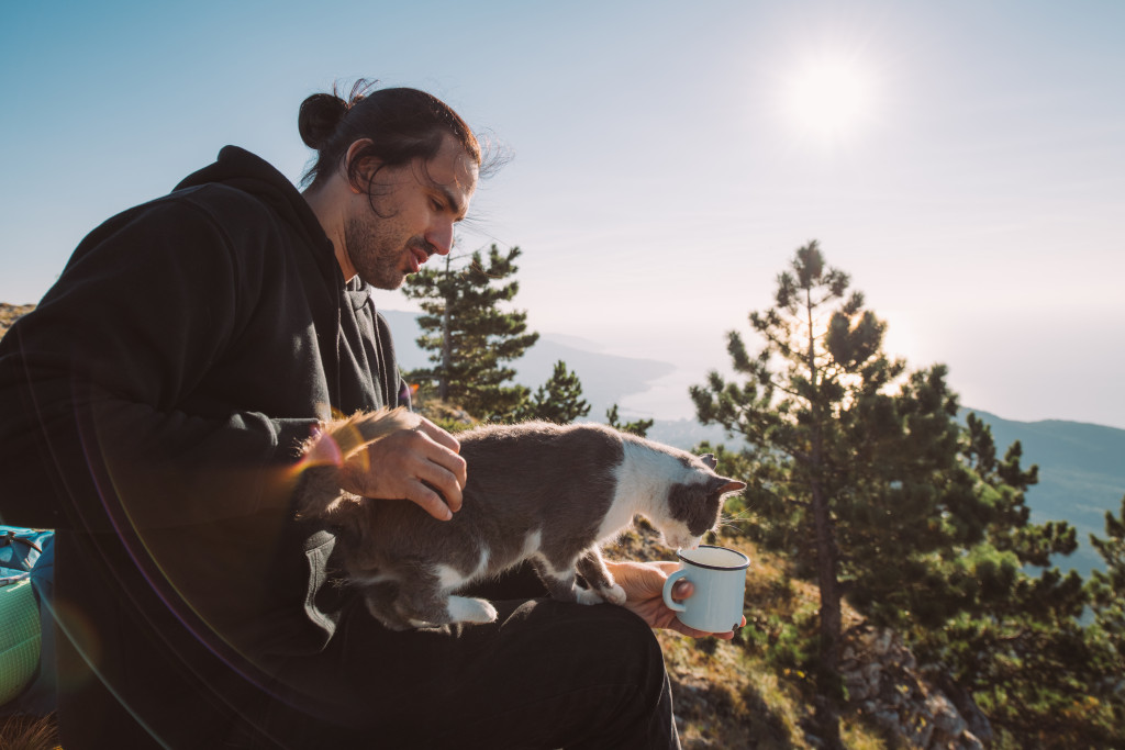 man sitting on top of mountain with pet cat drinking coffee